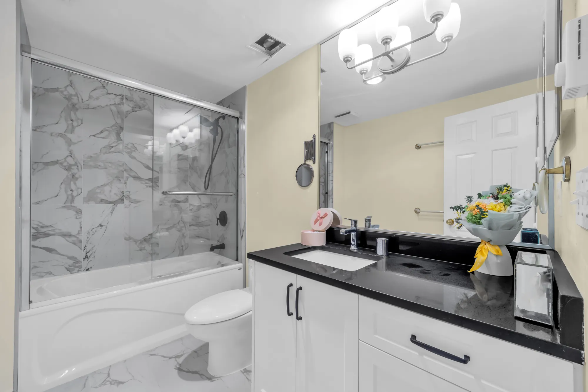 The same bathroom: the tub behind sliding glass doors, the vanity with a black counter, a mirror and light bar