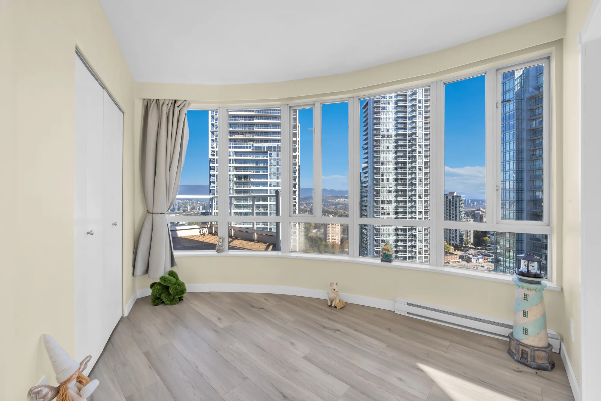 A bedroom with a curved wall of windows onto the towers, a curtain, a closet with white doors, a laminate floor, a few ornaments