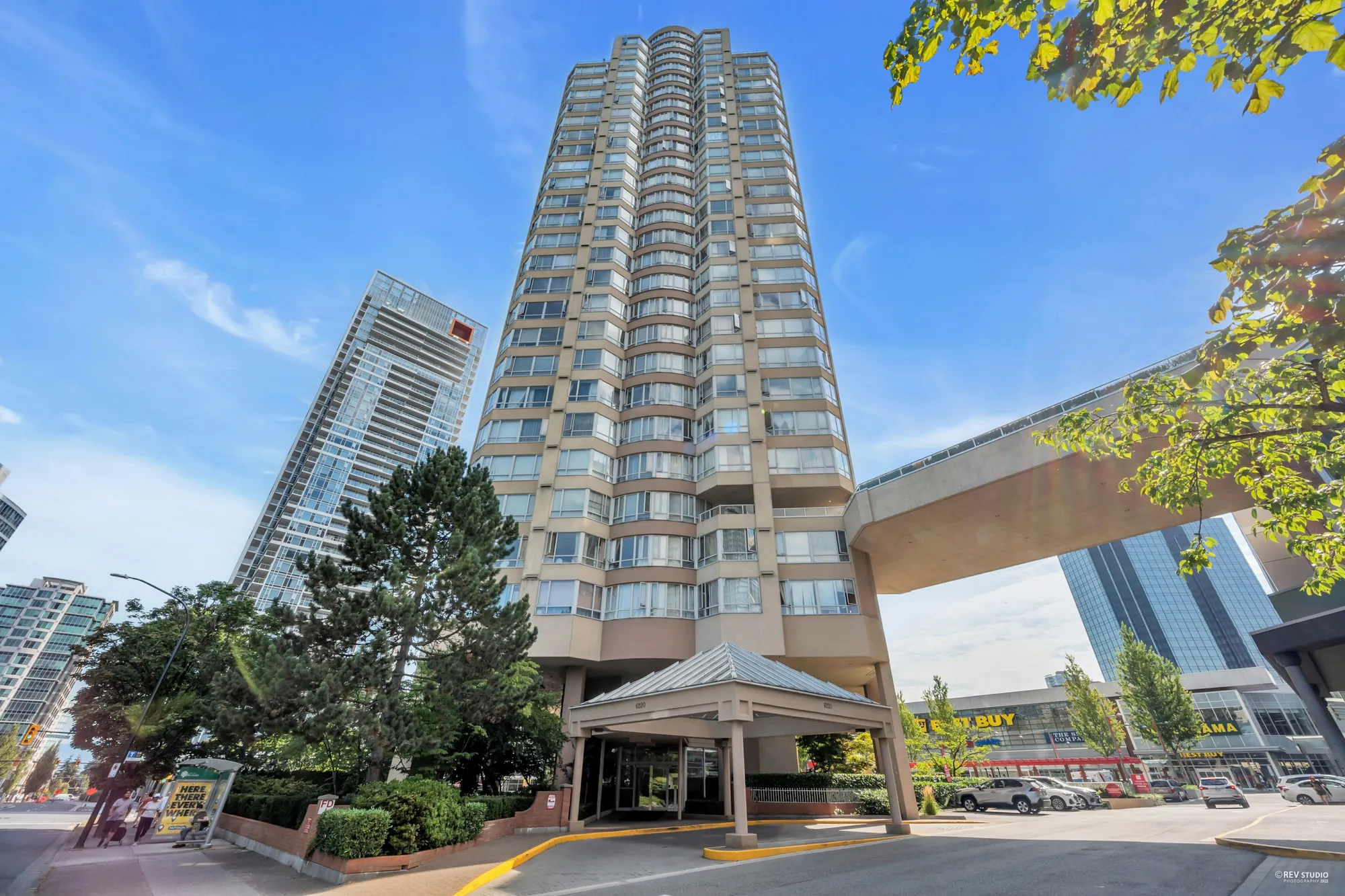 The tower from the street: a covered drop-off at the entrance, trees, glass towers beside it