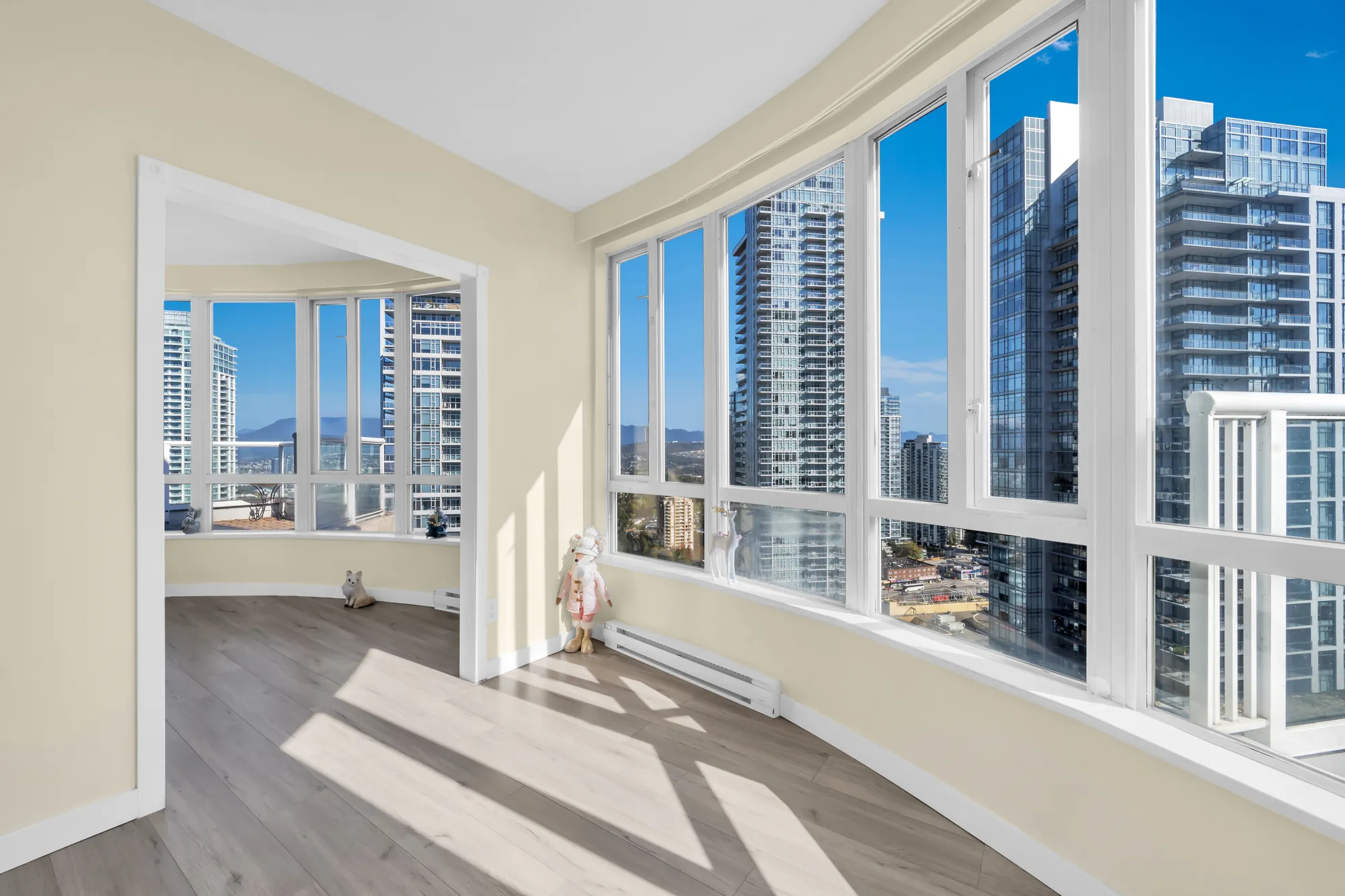 The wide opening between the two rooms behind the curved windows, sunlight on the laminate floor