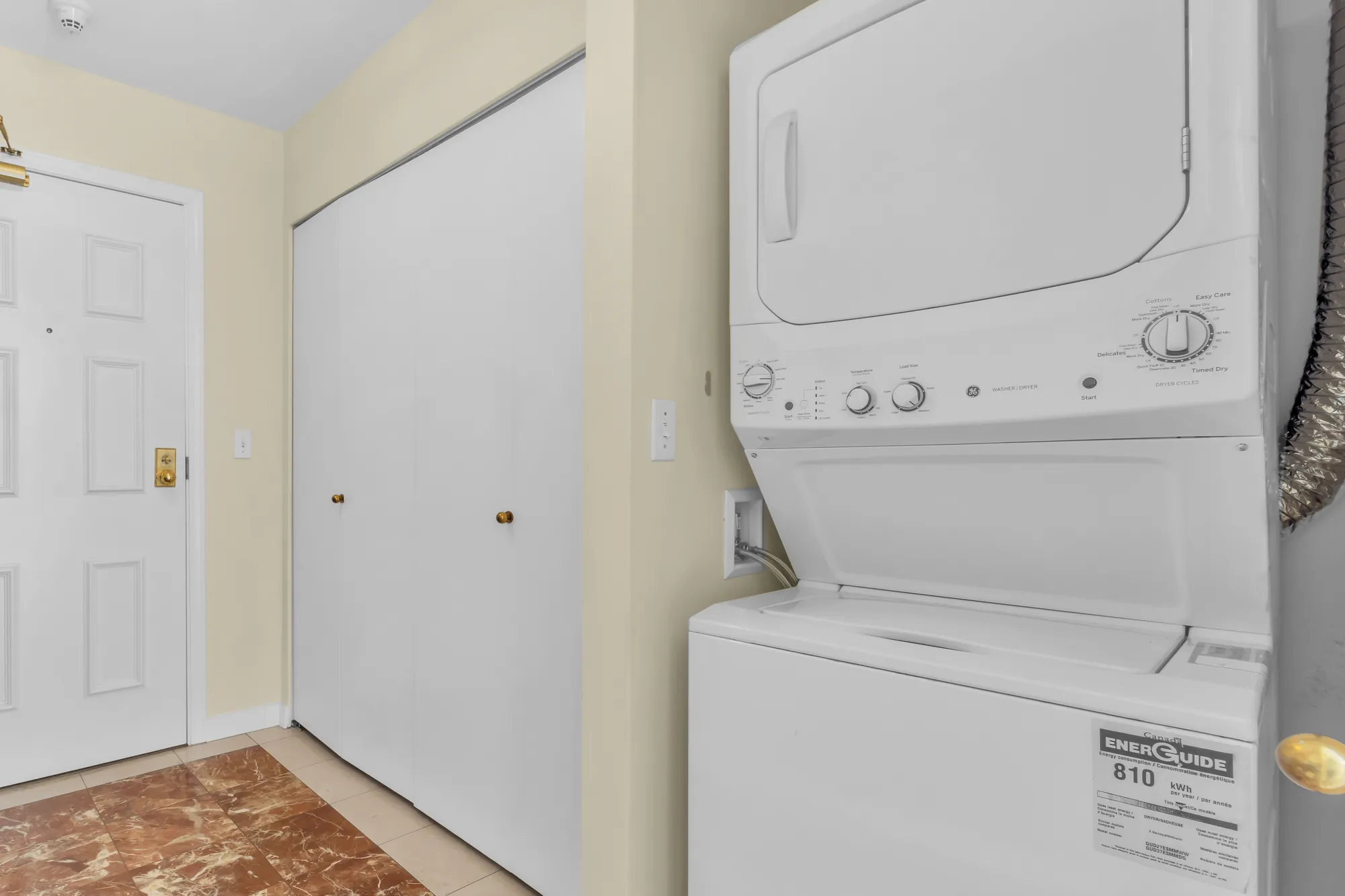 The entry: the front door, a double closet, a stacked washer and dryer, a marble-look tile floor