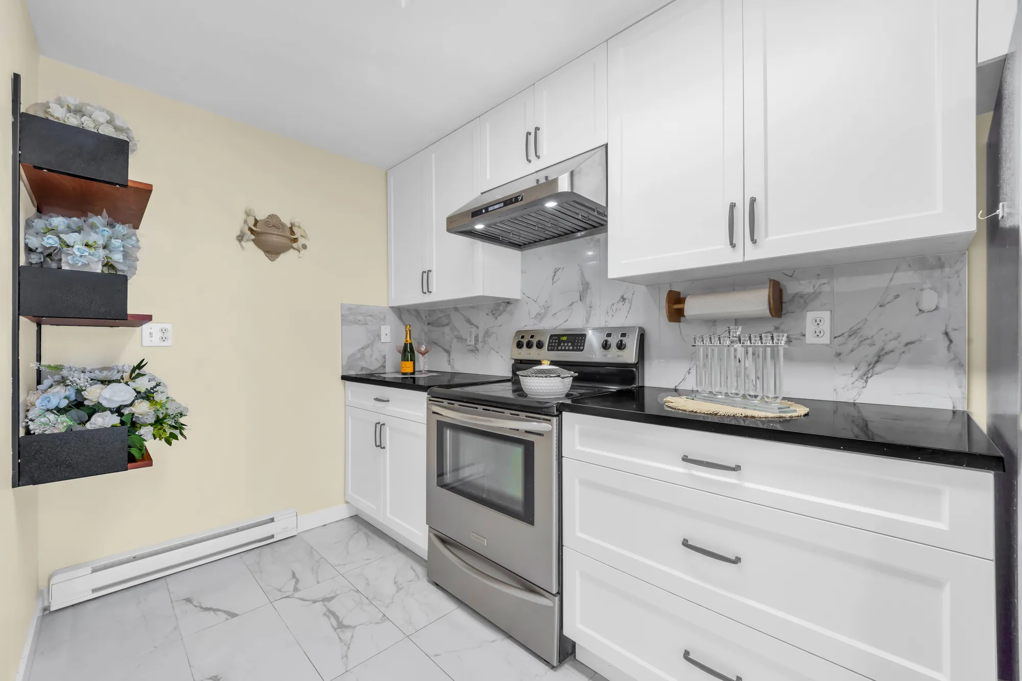 The range under a stainless hood, white cabinets, black counters, a marble-look backsplash, open shelves on the wall