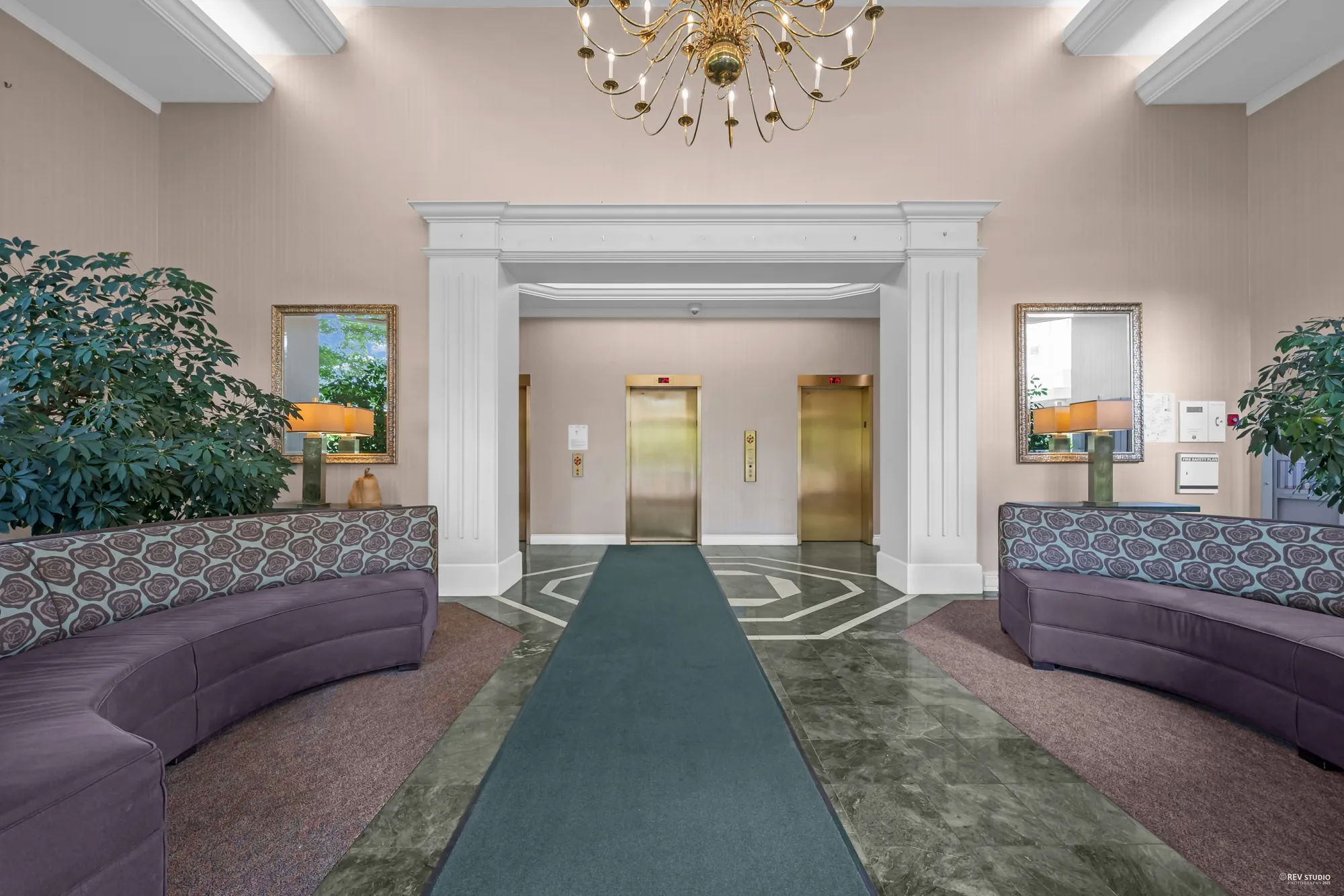 The lobby: two elevators behind white columns, purple banquettes, a crystal chandelier