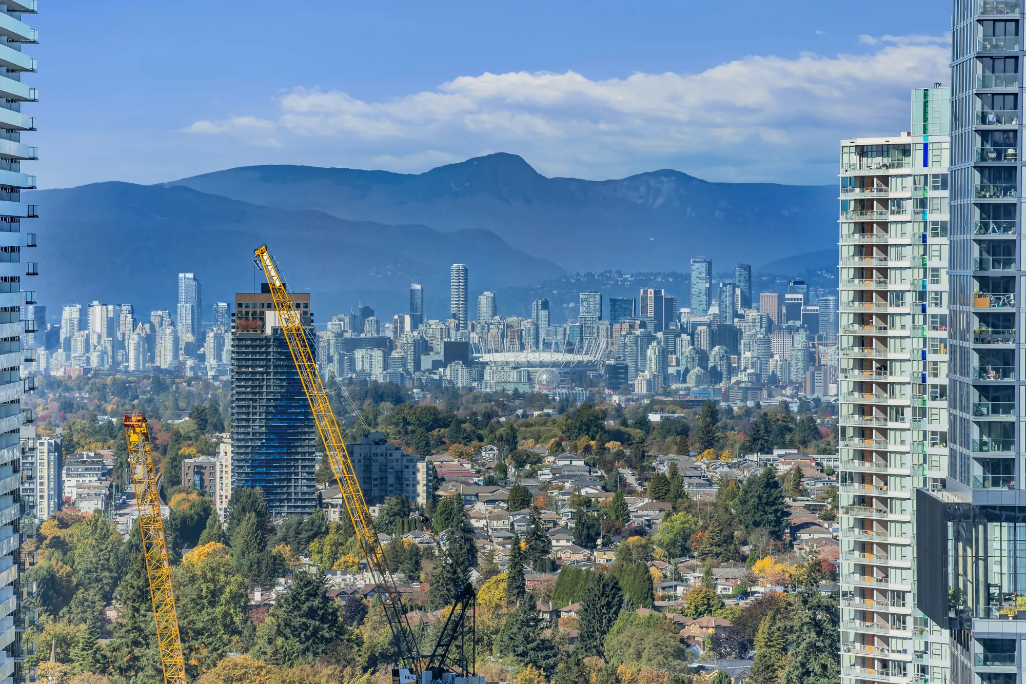 A long view to downtown Vancouver and the mountains behind it, cranes and towers in the foreground
